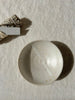 a top-down image of a neutral-coloured speckled ceramic dish with a white line through it with a sati smudge stick with a sati label visible in the background